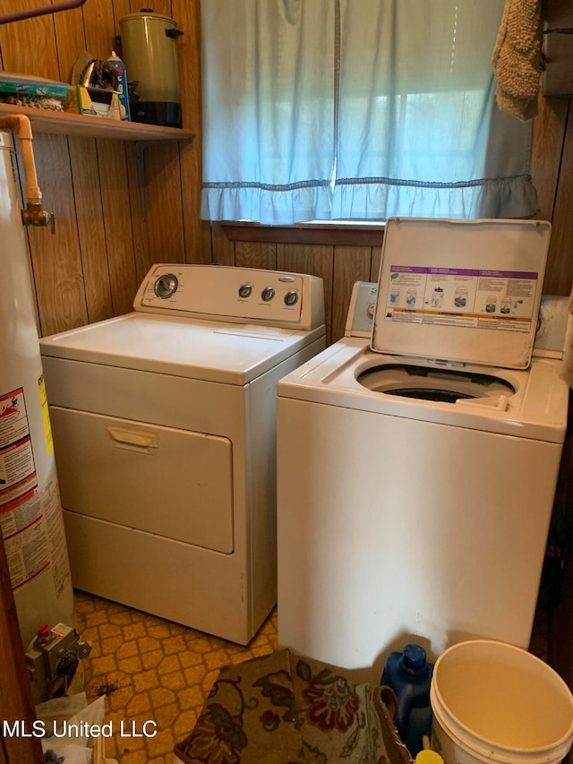 laundry area featuring water heater, washing machine and dryer, a healthy amount of sunlight, and wooden walls