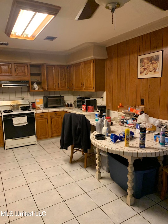 kitchen featuring white gas range, tile countertops, wooden walls, and a kitchen breakfast bar