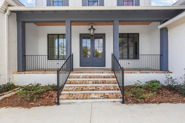 doorway to property featuring board and batten siding, a porch, french doors, and brick siding