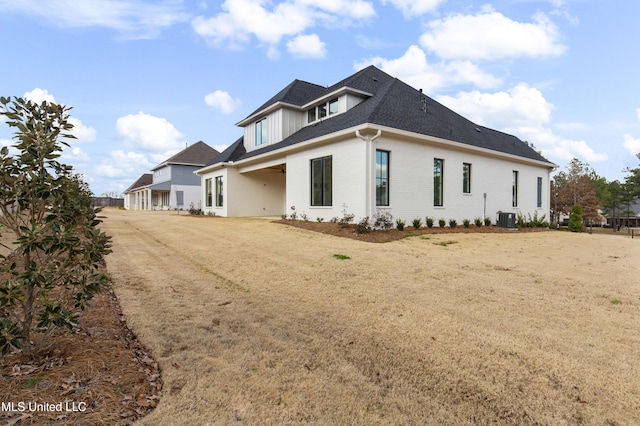 view of side of property featuring roof with shingles, a lawn, central AC, and brick siding