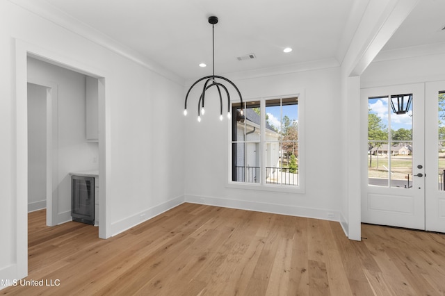 unfurnished dining area with beverage cooler, ornamental molding, light wood-style flooring, and baseboards