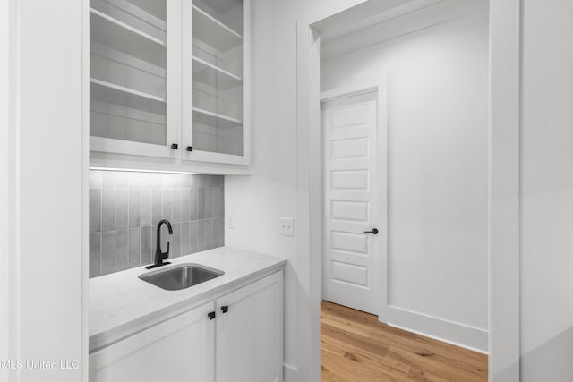 bar with tasteful backsplash, light wood-style flooring, and a sink