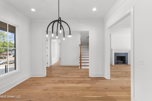 unfurnished dining area with a fireplace, baseboards, stairs, ornamental molding, and light wood finished floors