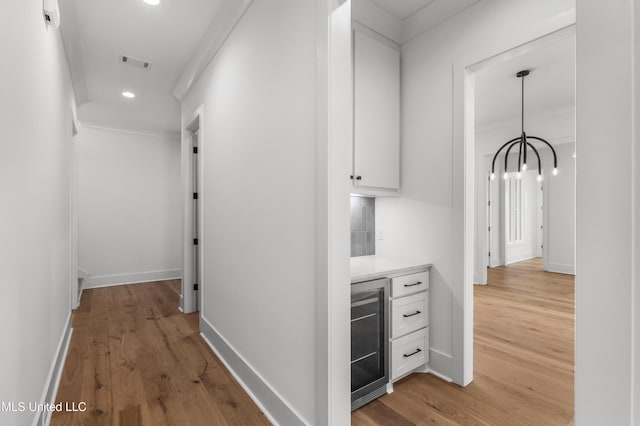 hallway with beverage cooler, visible vents, light wood-style flooring, and baseboards