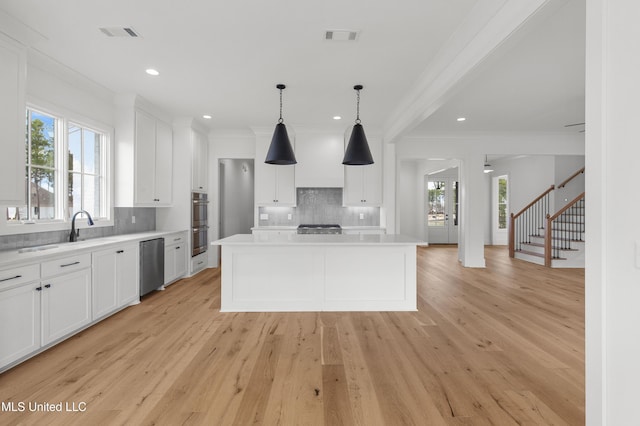 kitchen with a kitchen island, visible vents, white cabinetry, light countertops, and hanging light fixtures