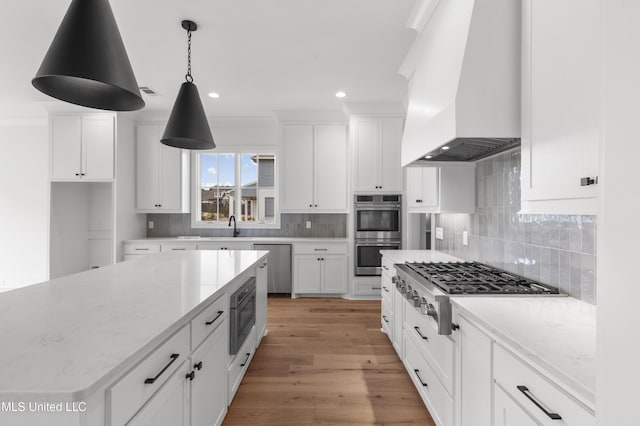 kitchen featuring light stone countertops, premium range hood, white cabinets, appliances with stainless steel finishes, and decorative backsplash