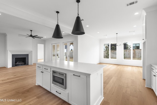 kitchen with visible vents, white cabinets, a kitchen island, stainless steel microwave, and open floor plan