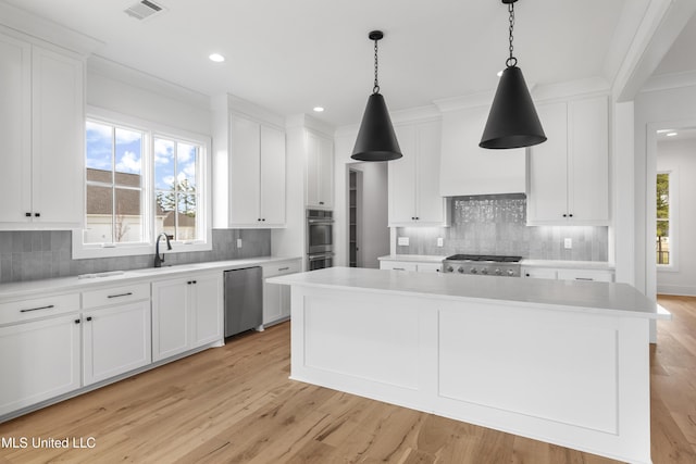 kitchen featuring white cabinets, a center island, hanging light fixtures, stainless steel appliances, and light countertops