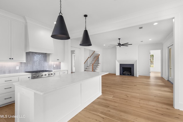 kitchen featuring a center island, white cabinetry, custom range hood, and decorative light fixtures