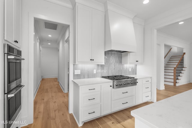 kitchen featuring appliances with stainless steel finishes, custom exhaust hood, white cabinetry, and decorative backsplash