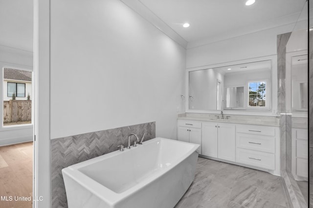 bathroom featuring a soaking tub, vanity, crown molding, and recessed lighting