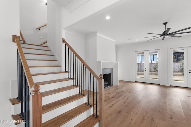 stairway with a fireplace, wood finished floors, baseboards, ornamental molding, and french doors