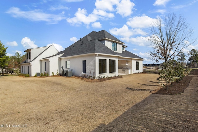 rear view of house featuring a shingled roof, a lawn, cooling unit, and brick siding