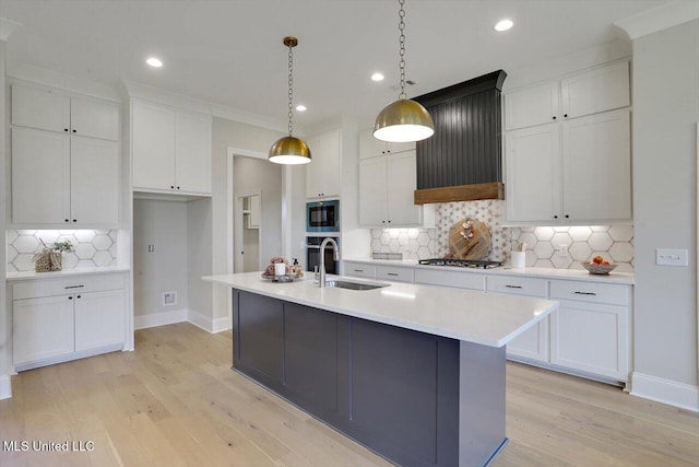 kitchen with white cabinetry, tasteful backsplash, a sink, built in microwave, and light wood finished floors