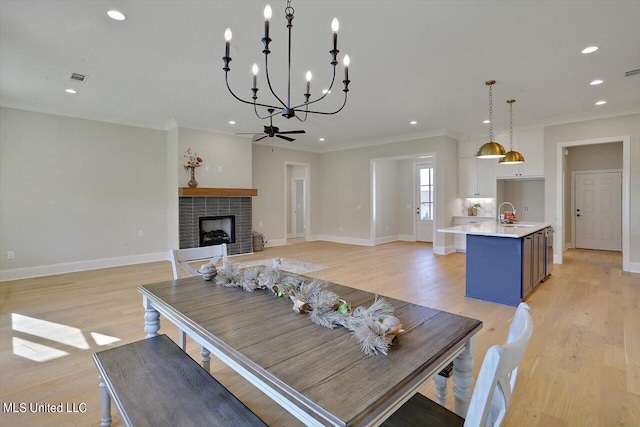 living room with light hardwood / wood-style flooring, sink, crown molding, a fireplace, and ceiling fan with notable chandelier