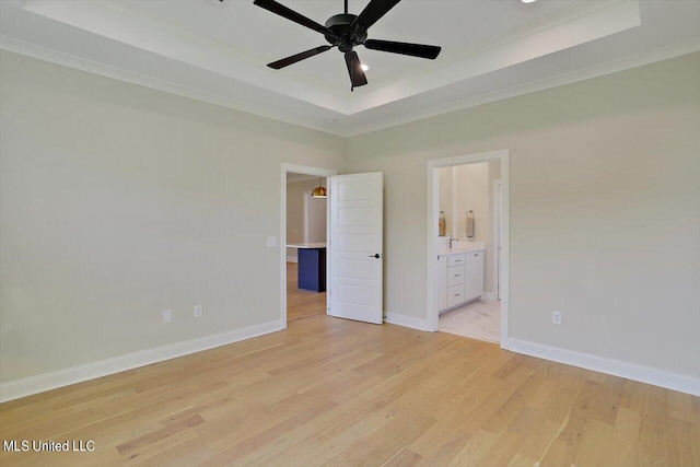 unfurnished bedroom featuring ensuite bathroom, a raised ceiling, light wood-type flooring, and ceiling fan