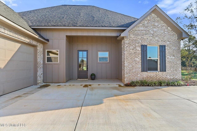 exterior space featuring board and batten siding, brick siding, driveway, roof with shingles, and an attached garage