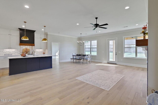 living room featuring sink, crown molding, ceiling fan with notable chandelier, and light wood-type flooring