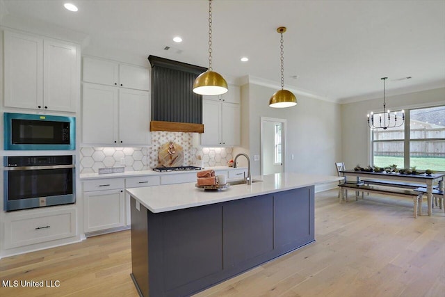 kitchen featuring white cabinets, hanging light fixtures, appliances with stainless steel finishes, light hardwood / wood-style flooring, and ornamental molding