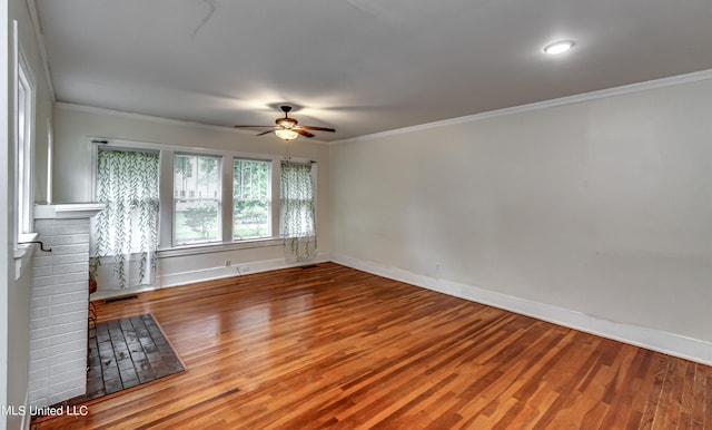 unfurnished room with crown molding, a brick fireplace, wood-type flooring, and ceiling fan