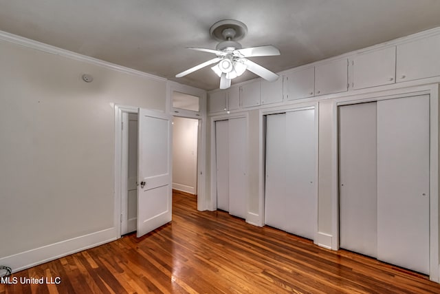 unfurnished bedroom featuring ornamental molding, ceiling fan, two closets, and dark hardwood / wood-style flooring