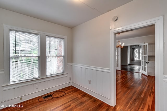 empty room featuring dark wood-type flooring, a notable chandelier, and a healthy amount of sunlight