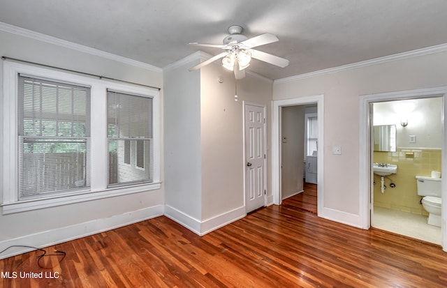 empty room with dark wood-type flooring, crown molding, tile walls, and ceiling fan