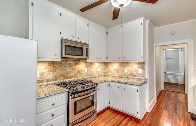 kitchen featuring decorative backsplash, white cabinets, ceiling fan, appliances with stainless steel finishes, and light wood-type flooring