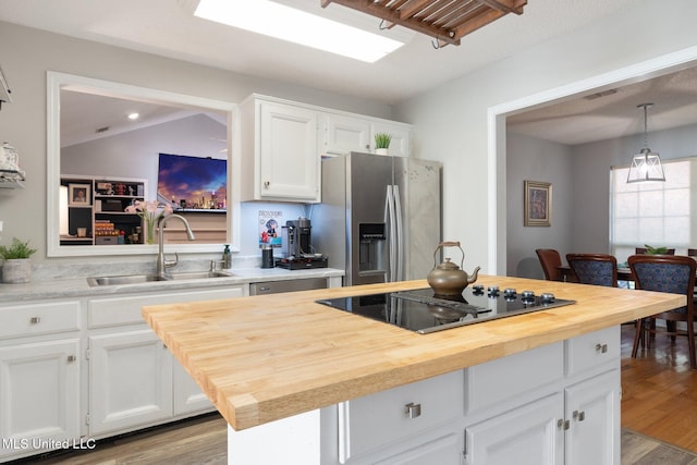 kitchen featuring white cabinets, stainless steel fridge with ice dispenser, black electric stovetop, sink, and decorative light fixtures