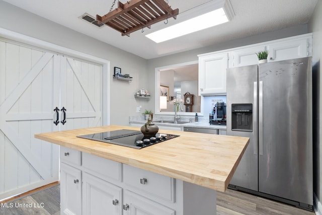 kitchen with white cabinets, light wood-type flooring, wooden counters, black electric cooktop, and stainless steel fridge