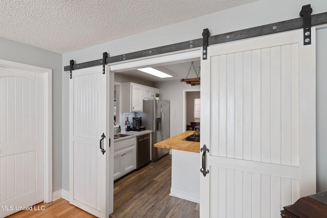 kitchen with sink, a textured ceiling, white cabinetry, hardwood / wood-style flooring, and appliances with stainless steel finishes