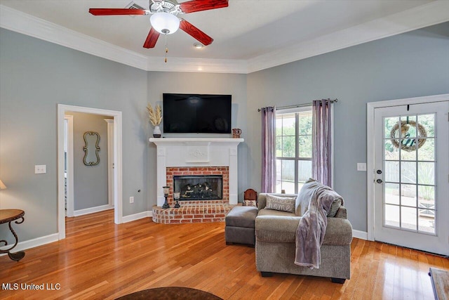 living room with crown molding, a fireplace, light hardwood / wood-style floors, and ceiling fan