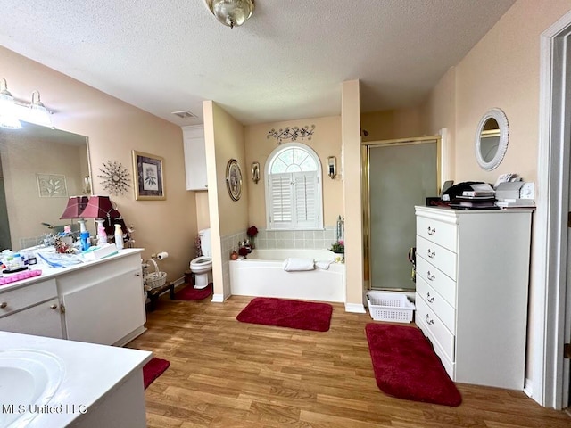 full bathroom with hardwood / wood-style flooring, toilet, separate shower and tub, vanity, and a textured ceiling