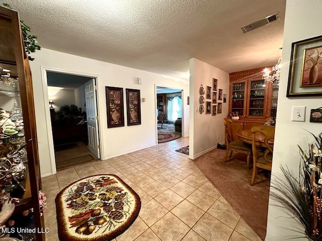 corridor featuring a textured ceiling, a chandelier, and light tile patterned floors