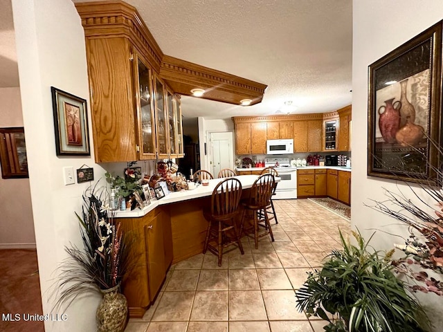 kitchen with a breakfast bar area, kitchen peninsula, light tile patterned flooring, a textured ceiling, and white appliances