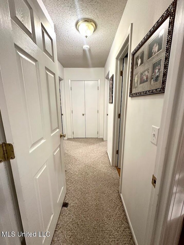 corridor with a textured ceiling and light colored carpet