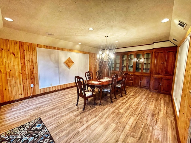 dining room with wood walls, light wood-type flooring, a textured ceiling, lofted ceiling, and a chandelier