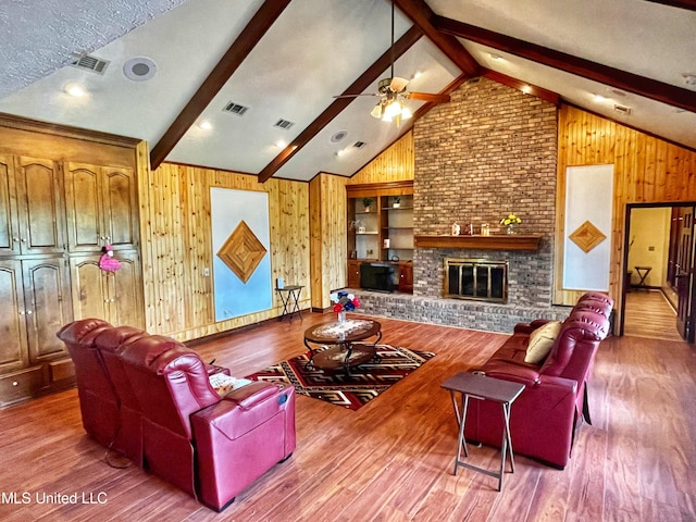 living room featuring vaulted ceiling with beams, wooden walls, hardwood / wood-style floors, a fireplace, and ceiling fan