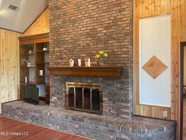 unfurnished living room featuring wood walls, wood-type flooring, a textured ceiling, a brick fireplace, and vaulted ceiling