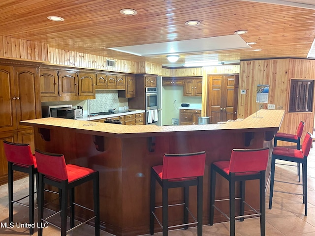 kitchen with a breakfast bar, wood ceiling, tasteful backsplash, and wood walls