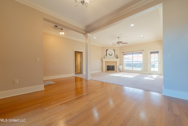 unfurnished living room featuring light wood-type flooring, a glass covered fireplace, crown molding, decorative columns, and baseboards