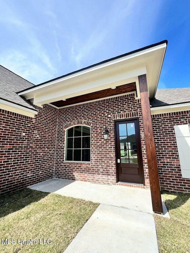 113 River Bend Ave, Vidalia, LA 71373 - view of exterior entry with a patio area, roof with shingles, a lawn, and brick siding