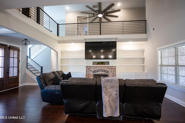 living room with a towering ceiling, dark hardwood / wood-style flooring, a brick fireplace, and built in shelves