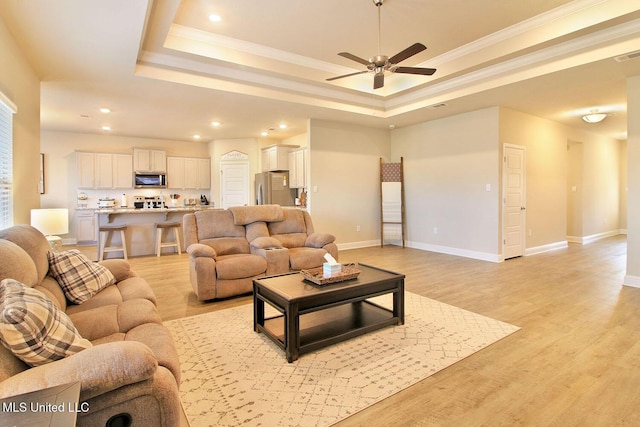 living room featuring crown molding, a tray ceiling, light hardwood / wood-style flooring, and ceiling fan