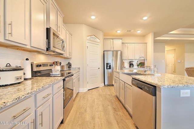 kitchen featuring sink, appliances with stainless steel finishes, a kitchen island with sink, tasteful backsplash, and light hardwood / wood-style floors