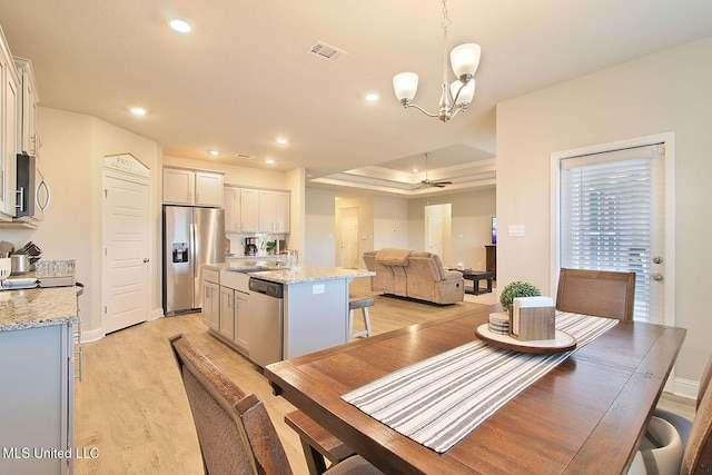 dining room with a raised ceiling, sink, ceiling fan with notable chandelier, and light hardwood / wood-style floors