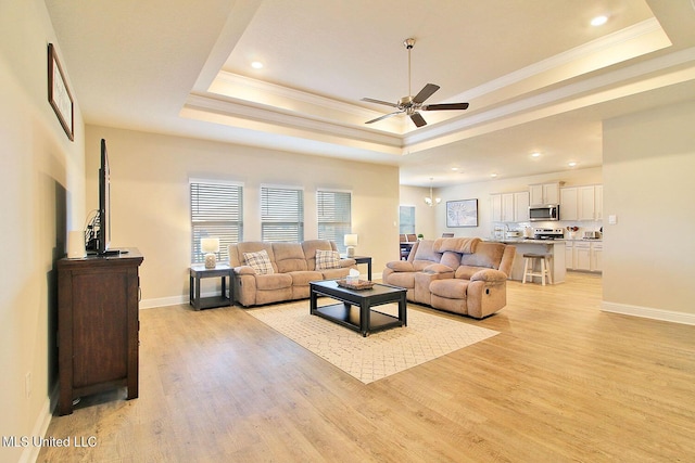 living room featuring crown molding, ceiling fan with notable chandelier, light hardwood / wood-style floors, and a tray ceiling