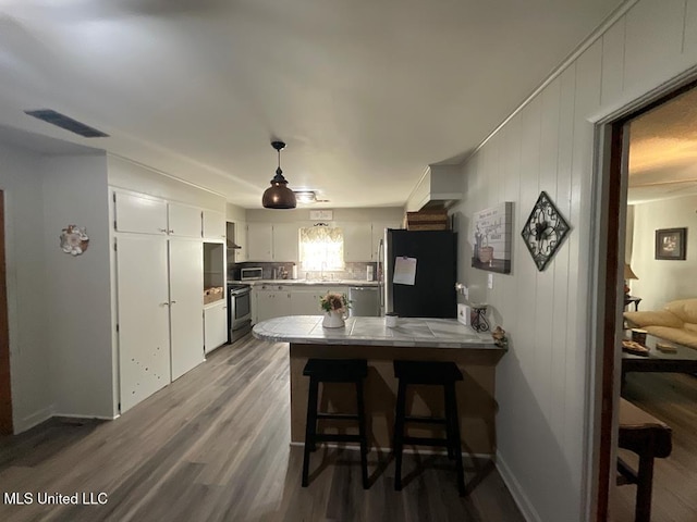 kitchen with kitchen peninsula, dark wood-type flooring, black appliances, pendant lighting, and white cabinetry