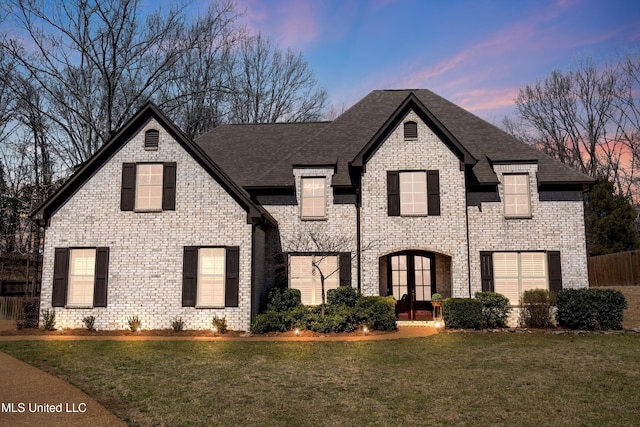 french country inspired facade featuring brick siding, french doors, a front yard, and roof with shingles