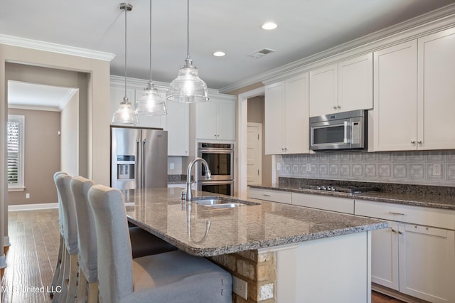 kitchen with visible vents, an island with sink, ornamental molding, decorative backsplash, and appliances with stainless steel finishes